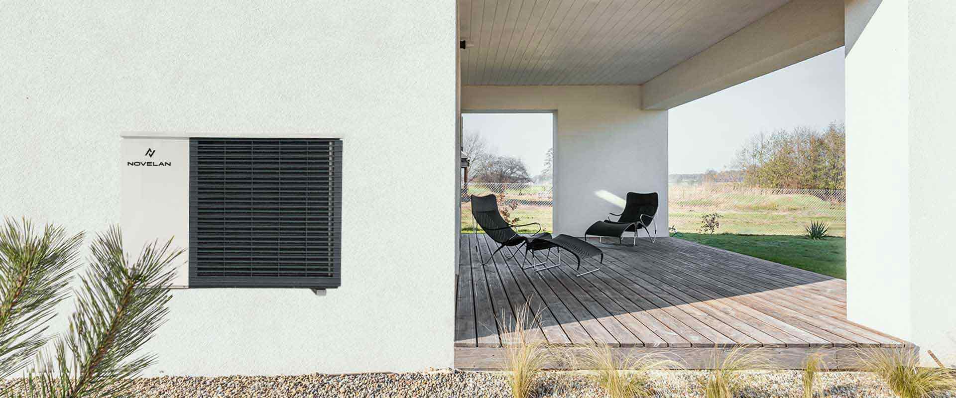 An air source heat pump is installed on a wall, above some decorative gravel and on the right, there is a terrace on the right with two sunbeds standing there.