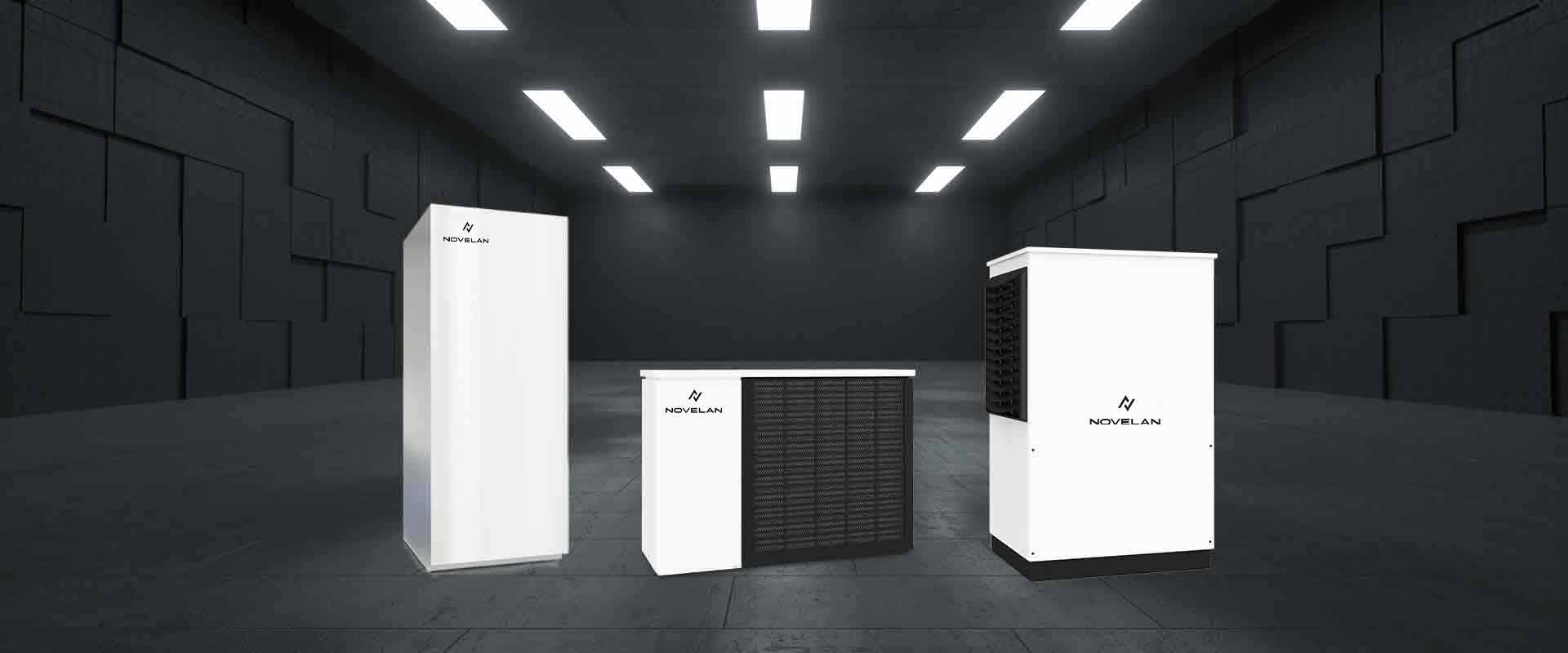 Three different types of NOVELAN heat pumps are standing next to each other inside a dark room with dimmed lights.