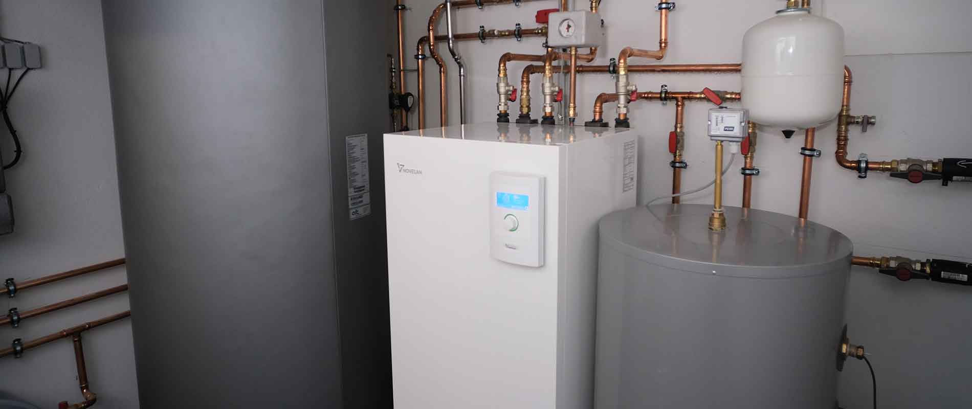 The WSV heat pump stands inside the boiler room, with puffer tanks on both sides and pipes extending on and inside the wall behind.