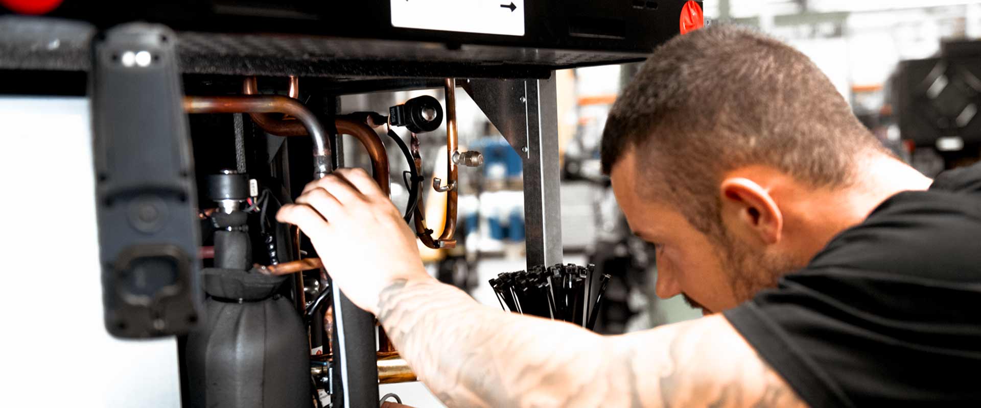 An employee can be seen in close-up while working on an open heat pump and adjusting the pipes inside.