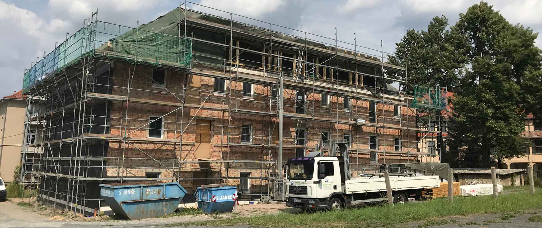 A new apartment building in construction is surrounded by scaffolding as a truck stands in front and a tree on the right side of the building.